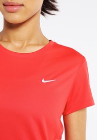 Camiseta deportiva roja de manga corta con cuello redondo, hecha de tela ligera, con un pequeño logo blanco de Nike en forma de swoosh en el pecho.