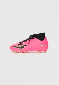 Cizma de fotbal roz aprins cu sireturi negre și guler pentru gleznă, cu bolțuri de talpă galben neon și logo-ul verde "SKX" pe lateral.