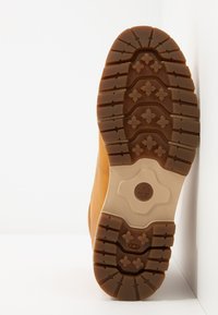Braune Gummistiefelsohle mit tiefen Profilmustern, einem auffälligen Logo und einer glatten beigen Zwischensohle. Robuste Bauweise ist sichtbar.