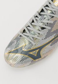 Zilveren en grijze voetbalschoenen met een textuurontwerp, voorzien van gouden accenten en een kenmerkend logo, en veters voor een stevige pasvorm.