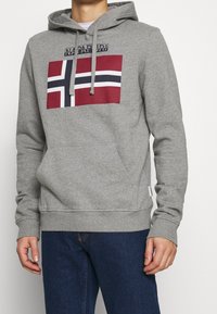Sudadera gris con bolsillo tipo canguro, presenta un diseño de bandera noruega en rojo y azul marino, incluye cordones y puños de canalé.