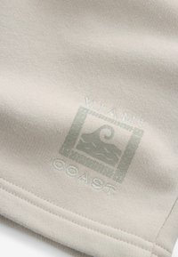 Kramsfarvet stof prydet med et logo med "MIAMI COAST" og et bølgemotiv, præget i en lidt mørkere nuance. Glat tekstur, let stræk.