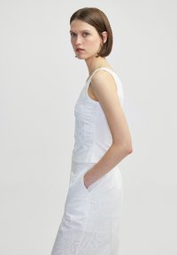 Weißes ärmelloses Oberteil mit besticktem Blumenmuster, kombiniert mit einem weißen Rock mit Lochmuster. Glatte Textur, figurbetontes Design.