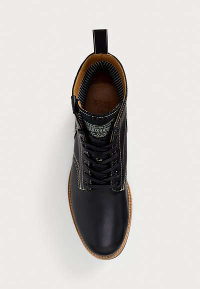 Stivale in pelle nera con lacci, suola beige, cuciture bianche, fodera interna a righe e etichetta con marchio sulla linguetta.