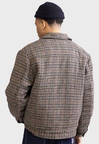 Veste à carreaux marron et gris avec un col, tissu texturé et manches longues ; la vue arrière montre des coutures verticales et un ourlet à côtes.