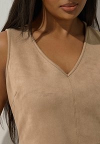 Beżowa zamszowa bluzka bez rękawów z dekoltem w kształcie litery V, o gładkiej teksturze i minimalnych detalach przeszycia, podkreślająca czysty design odzieży.