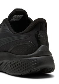 Schwarzer Sportschuh mit einer strukturierten Stoffoberfläche, verstärkter Ferse und einer gebogenen Sohle mit sichtbaren Traktionsmustern. Logo an der Ferse.