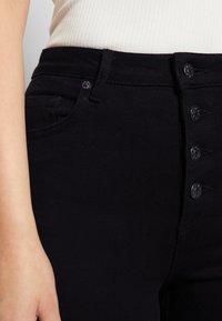 Calças de ganga pretas de cintura alta com uma textura suave, apresentando um fecho de cinco botões, bolsos frontais e detalhes de costura discretos.