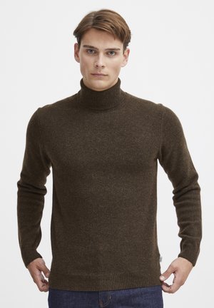 Brauner Rollkragenpullover aus einem weichen, strukturierten Stoff mit langen Ärmeln und gerippten Bündchen und Saum, kombiniert mit blauen Jeans.