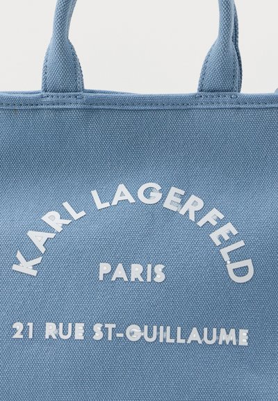 Синя платнена торба с бял надпис "KARL LAGERFELD PARIS 21 RUE ST-GUILLAUME" и две къси дръжки.
