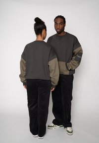 Dark gray oversized sweatshirt with light green accents, paired with black corduroy pants. Displayed on two models from front and back.