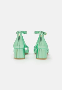 Mintgröna blockklackade sandaler i glänsande lädermaterial, med ankelremmar och detaljer i guldton. Stängd häl och öppen tå-design.