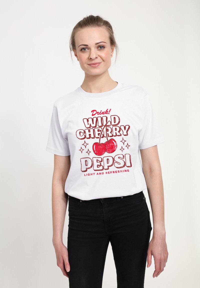 Bílá bavlněná tričko s červeným grafickým designem, na kterém jsou třešně a text "WILD CHERRY PEPSI." Černé džíny doplňují outfit.