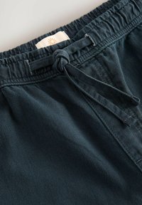 Mørkegrønne fløjelsshorts med elastisk talje og snoretræk samt en lille stoflabel med et sol-logo nær toppen.