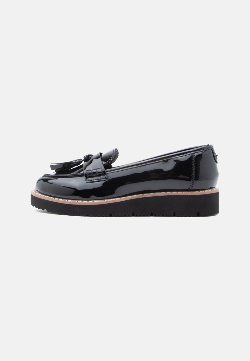 Mocassin en cuir noir brillant avec détails à pampilles et semelle épaisse en caoutchouc noir, présenté de profil sur fond blanc.