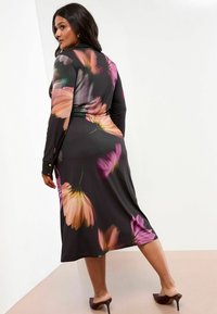 Schwarzes Blumenkleid mit langen Ärmeln, das große rosa und lila Blumenmuster aufweist. Glatter Stoff und knielang. Absätze runden den Look ab.