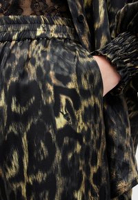 Gros plan sur une jupe noire et dorée à imprimé animalier, taille élastique et manche de veste assortie avec un poignet froncé, main dans la poche.
