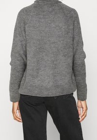 Grauer Strickpullover mit hohem Kragen, geripptem Saum und Raglanärmeln. Der Stoff hat eine weiche Textur und subtile Farbvariationen.