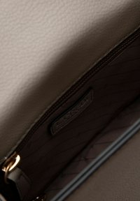 De binnenkant van de beige leren handtas heeft een gladde textuur, een ritssluiting en een merklabel met een gewatteerde voering in een donkerder tint.