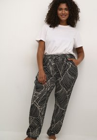 Schwarz-weiße gemusterte Hose mit einem Blättersujet, elastischem Bund, Seitentaschen und einem lockeren Schnitt, kombiniert mit einem schlichten weißen T-Shirt.