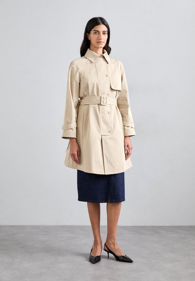 Beige trench coat s páskem v oblasti pasu, velkými knoflíky a bočními kapsami. Kombinováno s tmavou džínsovou sukní a černými lodičkami se špičatou špičkou.