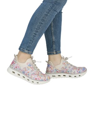 Personne portant un jean bleu et des chaussures de sport blanches avec des motifs floraux colorés et des semelles épaisses.