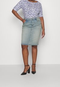 Blommig topp med korta ärmar, tillsammans med en figurnära, knälång ljusblå jeanskjol. Svarta högklackade skor med vristband.