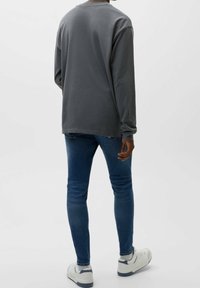 Šedá košile s dlouhým rukávem a kulatým výstřihem, zkombinovaná s úzkými modrými džíny a bílými teniskami. Jednoduchý, ležérní design bez dalších vzorů.