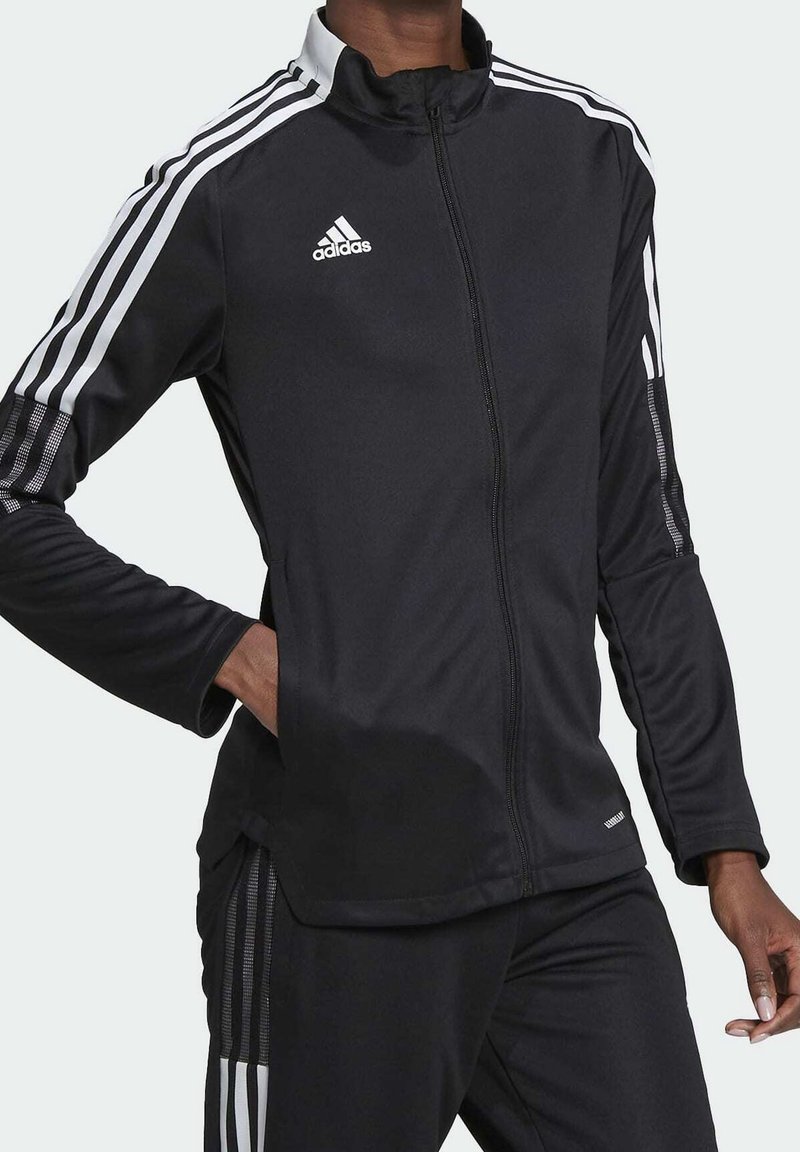 Černá zipová sportovní bunda vyrobená z hladkého materiálu. Obsahuje bílé trojité pruhy na rukávech a zvýšený límec. Logo Adidas na hrudi.