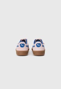 Scarpe in suede rosa con dettagli blu, suole piatte in gomma marrone e un logo Puma blu sul tallone. Caratterizzano un design semplice senza lacci.