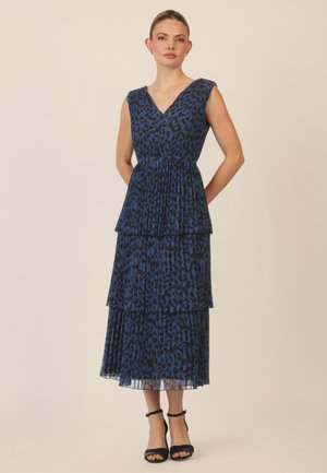 Abito a stampa leopardata blu con scollatura a V, design senza maniche, strati a pieghe sovrapposti e orlo alla caviglia. Indossato con tacchi neri con cinturini.