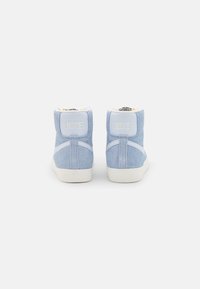 Wysokie sneakersy Nike z jasnoniebieskiego zamszu z białymi akcentami. Charakteryzują się teksturowanym materiałem i wyściełanym kołnierzem dla komfortu.