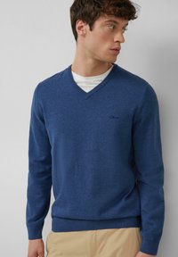 Niebieski sweter w serek, wykonany z miękkiego dzianiny. Posiada długie rękawy, prążkowany dół oraz małe haftowane logo na piersi.