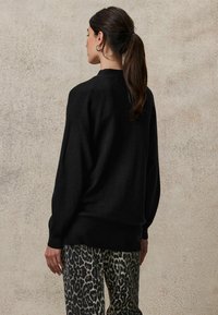 Svart stickad tröja med en lös passform, ribbat mönster och rundad nederkant, ihopparad med leopardmönstrade byxor med en slät yta.