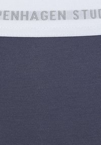 Marineblauwe stof met een ribbelstructuur en een witte tailleband met de tekst "COPENHAGEN STUDIOS" in het grijs, wat het merkonderscheid benadrukt.