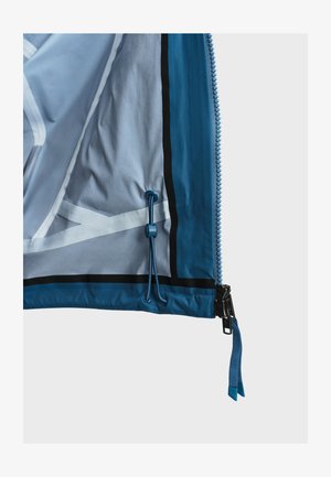 Borde de chaqueta azul mostrando cremallera con tirador y bloqueo de cordón ajustable en el dobladillo interior contra un fondo liso.