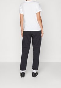 Biała koszulka z krótkim rękawem w połączeniu z ciemnoszarymi spodniami dresowymi. Spodnie mają ściągacze na nogawkach i luźny krój. Buty są czarne z białymi akcentami.