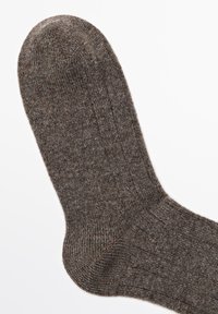 Hnědá ponožka s texturovaným vzorem, žebrovaným pletením, hladkým špičkovým zakončením a zesílenou patou, která představuje teplý a měkký materiál.