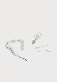 Zestaw trzech kolczyków: srebrny spiralny kółko, pojedynczy srebrny wkrętka z perłowym akcentem oraz cienki srebrny wzór na haczyku.