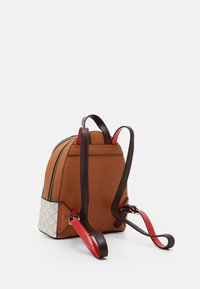 Brun läderryggsäck med en avsmalnande form, röda och bruna remmar och en mönstrad sidopanel. Har en dubbel dragkedjestängning.