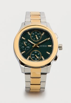 Two-tone metal wristwatch with black dial, gold accents, three subdials for day, date, and 24-hour time, labeled "GUESS."