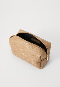 Trousse de maquillage beige texturée avec une fermeture éclair dorée, dotée d'un extérieur à motifs et d'une doublure intérieure noire. Détail du logo visible à l'avant.