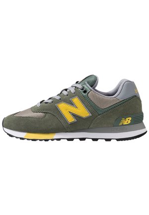 Grüner und grauer New Balance Sneaker mit gelbem Logo, grauen Schnürsenkeln, Mesh-Gewebe, Veloursleder-Details und weißer und schwarzer Sohle mit gelbem Akzent.