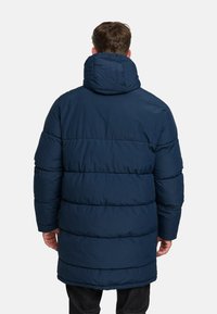 Navy blue puffer coat with a high collar, featuring horizontal quilted sections and long sleeves. Finishes below the hips for added warmth.