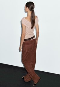 Lys pink off-shoulder top med samling, parret med brune ruskinds bredde bukser, der har et bredt sort bælte med sølvhardware.