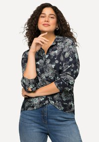 Camicia navale con stampa floreale e disegni in blu chiaro e bianco; maniche lunghe arrotolate, colletto, realizzata in tessuto liscio, abbinata a jeans blu.