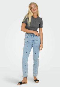 Grå kortærmet top, lyseblå jeans med sorte hjerte mønstre, afslappet pasform og sorte slidesandaler. Simpelt design med afslappet stil.