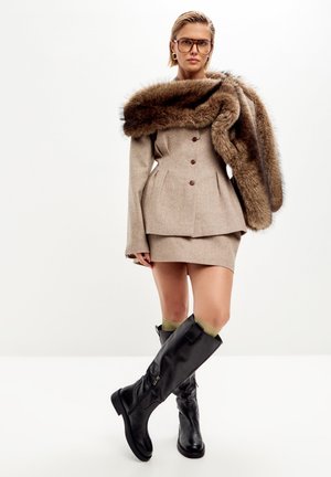 Beige skræddersyet frakke med pelskrave, parret med en beige mini-nederdel. Båret med knæhøje sorte læderstøvler og olivengrønne sokker.