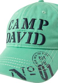 Green cotton cap featuring black embroidered text "CAMP DAVID" and a round stamp detail. The design includes visible stitching and texture.