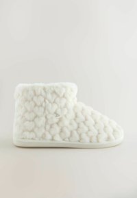 Witte faux fur pantoffel met een getextureerd hartpatroon, afgeronde vorm, zachte oppervlak en een witte zool met een merklabel.